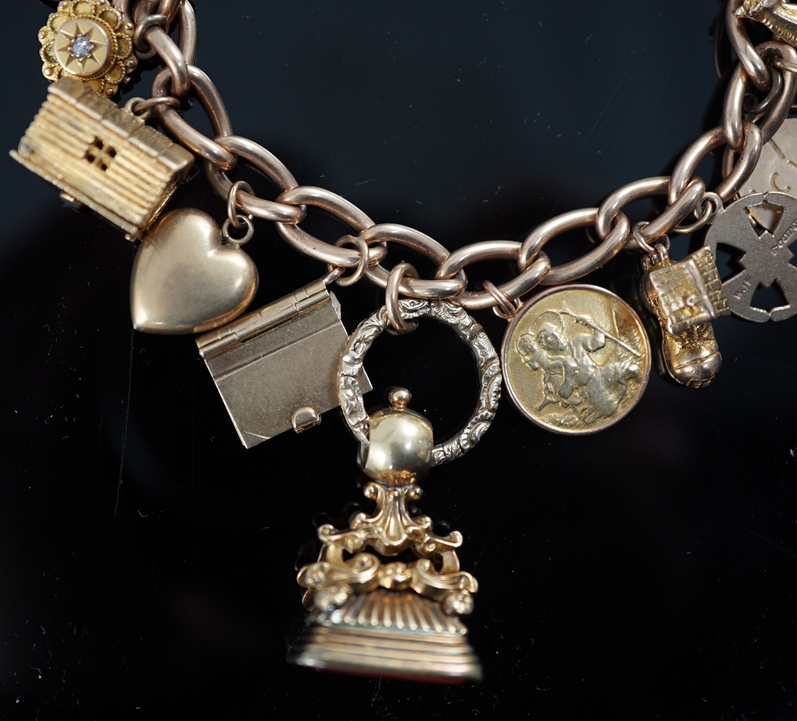 A 15ct? gold oval link charm bracelet, hung with seventeen assorted mainly 9ct charms